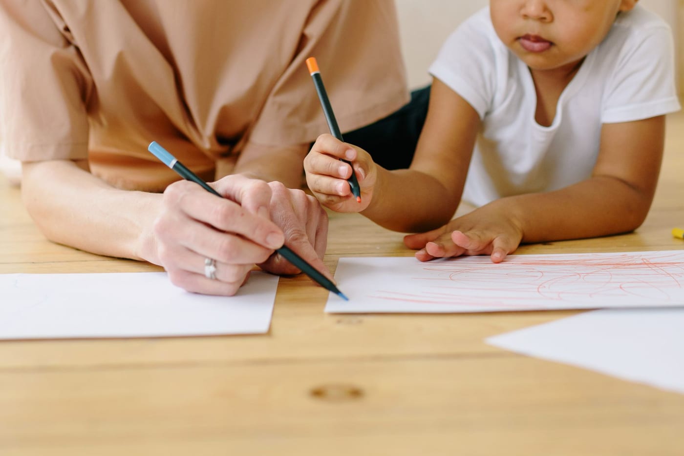An adult and a child drawing together with coloured pencils at a table